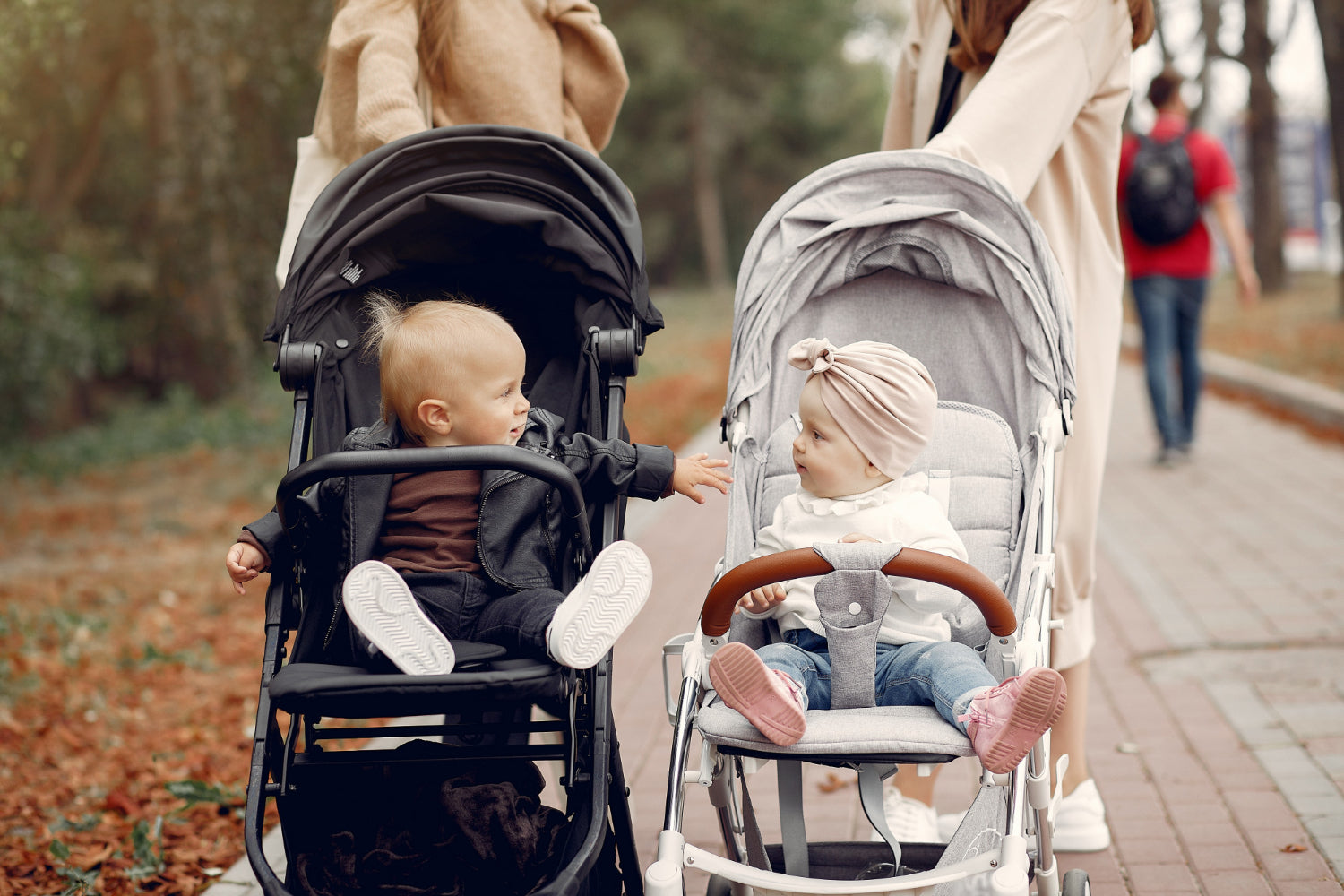 Two children in strollers with their parents in a park setting